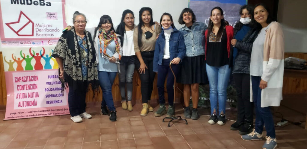 9 mujeres con y sin discapacidad, paradas posando para la foto al lado de un banner que dice Mudeba.